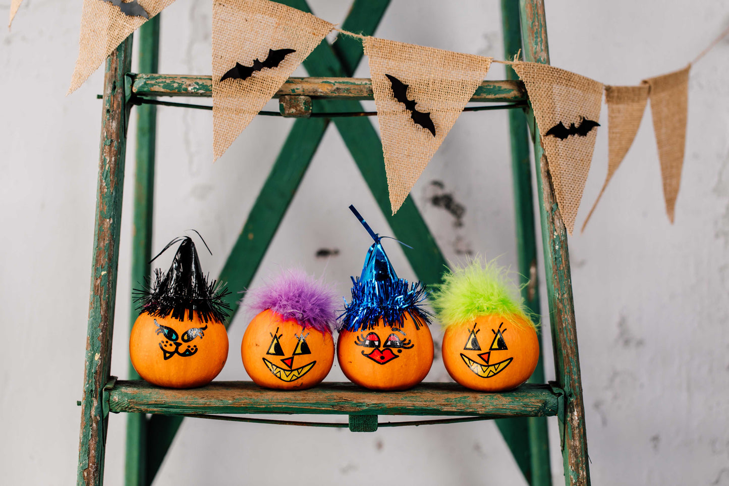 Decorative pumpkins with colorful faces on a green ladder with Halloween-themed bunting.
