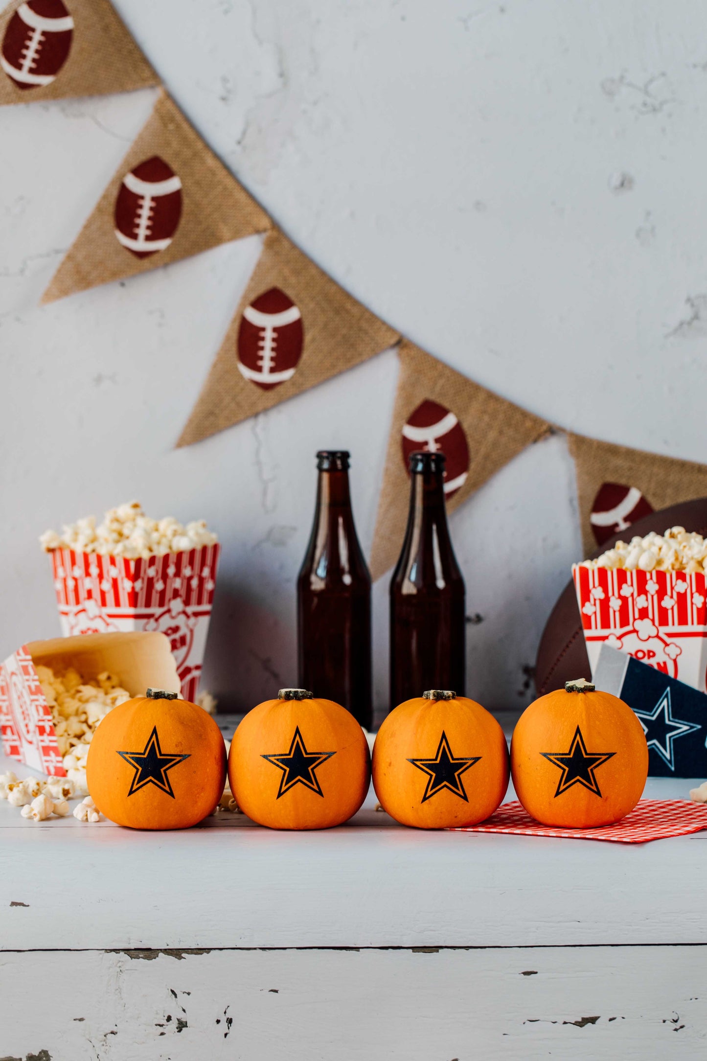 Four pumpkins with star designs on a table with popcorn and bottles, against a festive background.