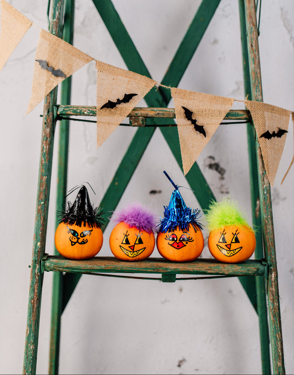 Decorative pumpkins with colorful faces on a green ladder with burlap banner