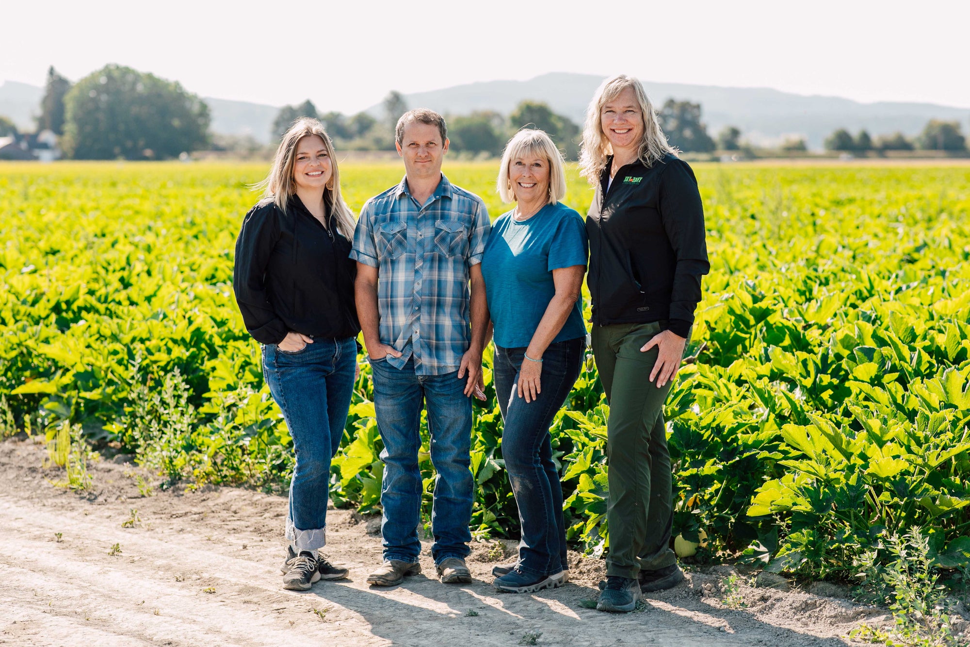 Four people standing in a field with greenery and mountains in the background