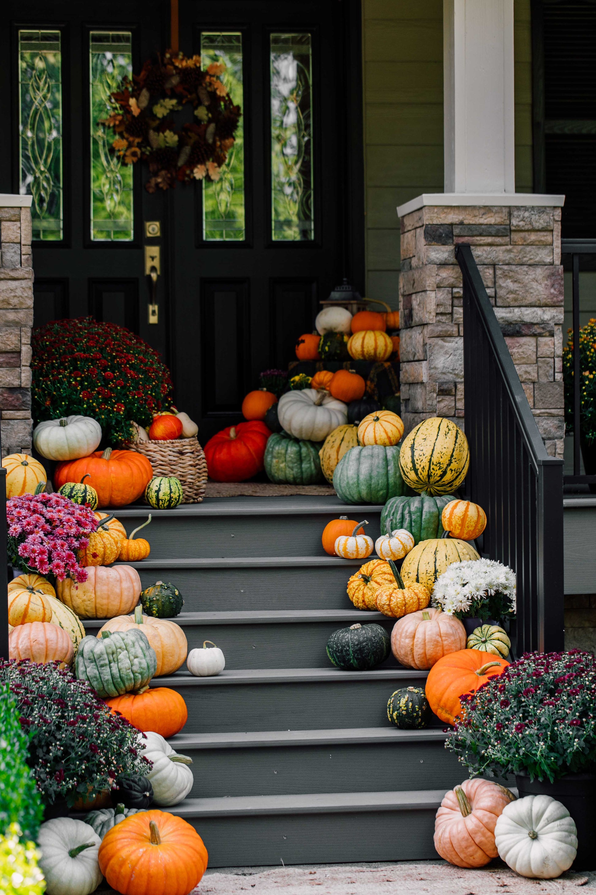 Decorative display of pumpkins and gourds on a staircase with a house in the background.