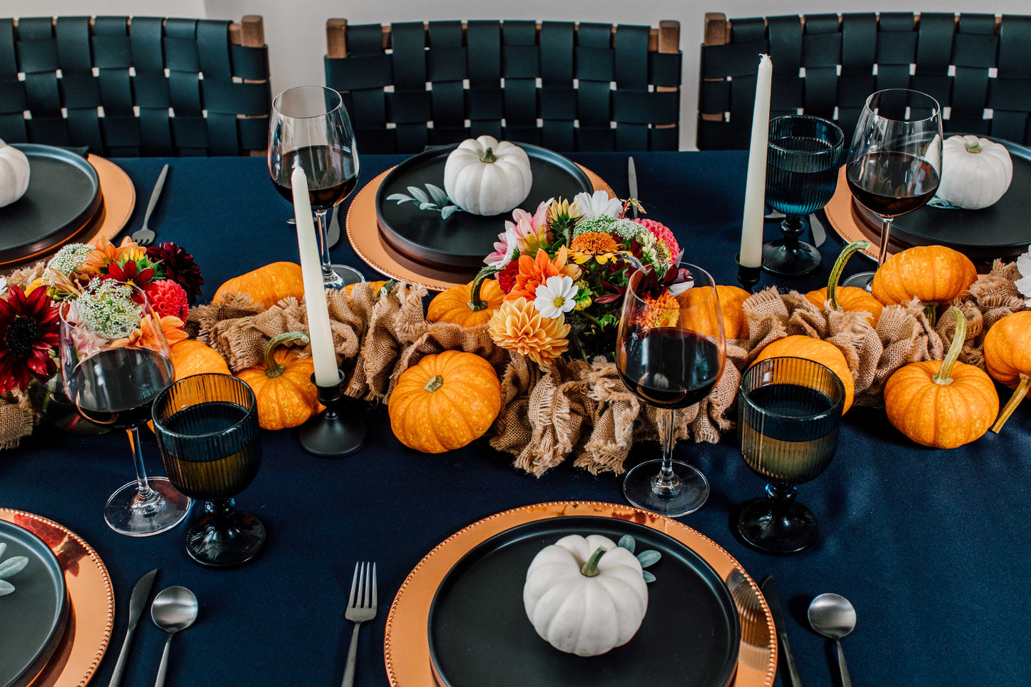 Halloween-themed table setting with pumpkins, candles, and decorative flowers on a dark blue tablecloth.