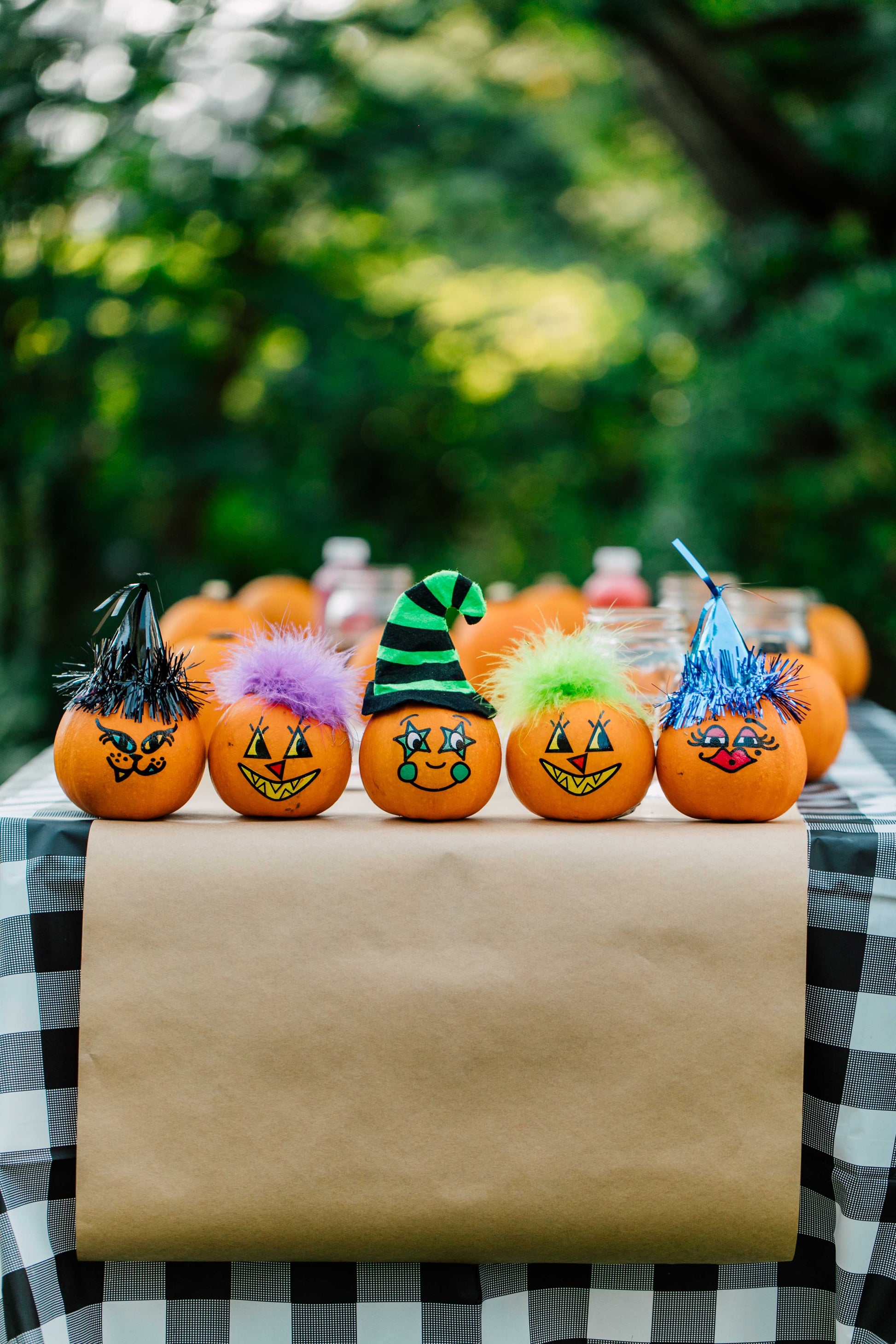 Decorative pumpkins with colorful hats on a checkered tablecloth outdoors.