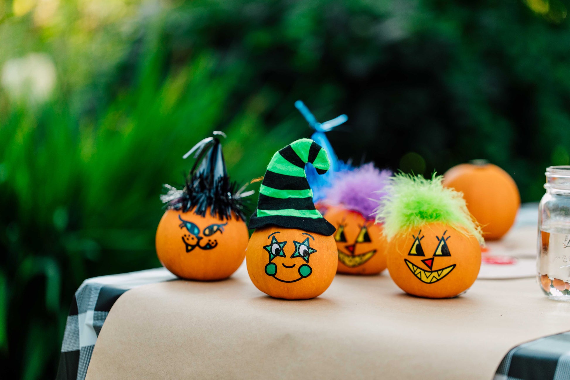Decorative pumpkins with painted faces and colorful hats on a table outdoors.