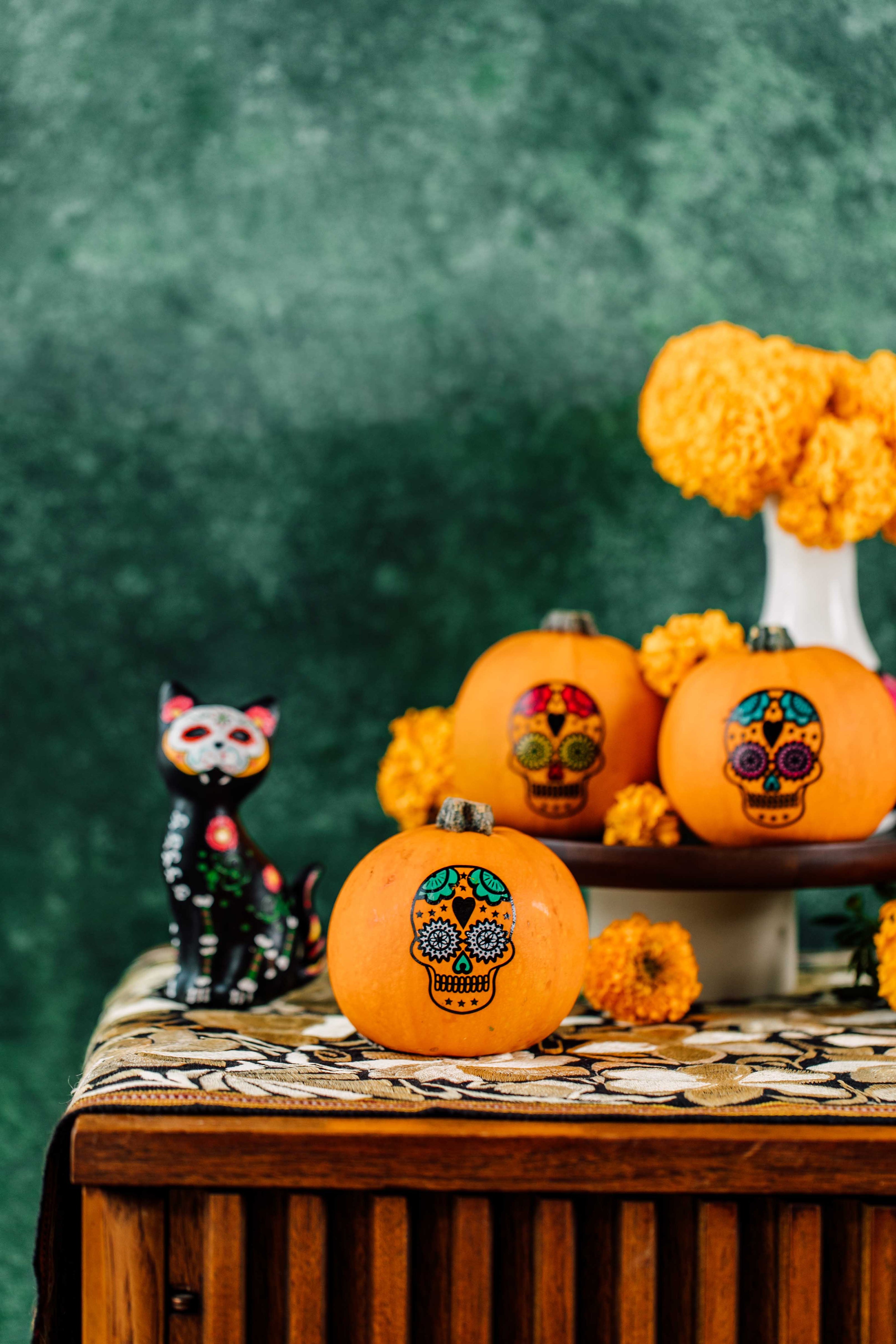 Decorative pumpkins with skull designs on a table with a green background