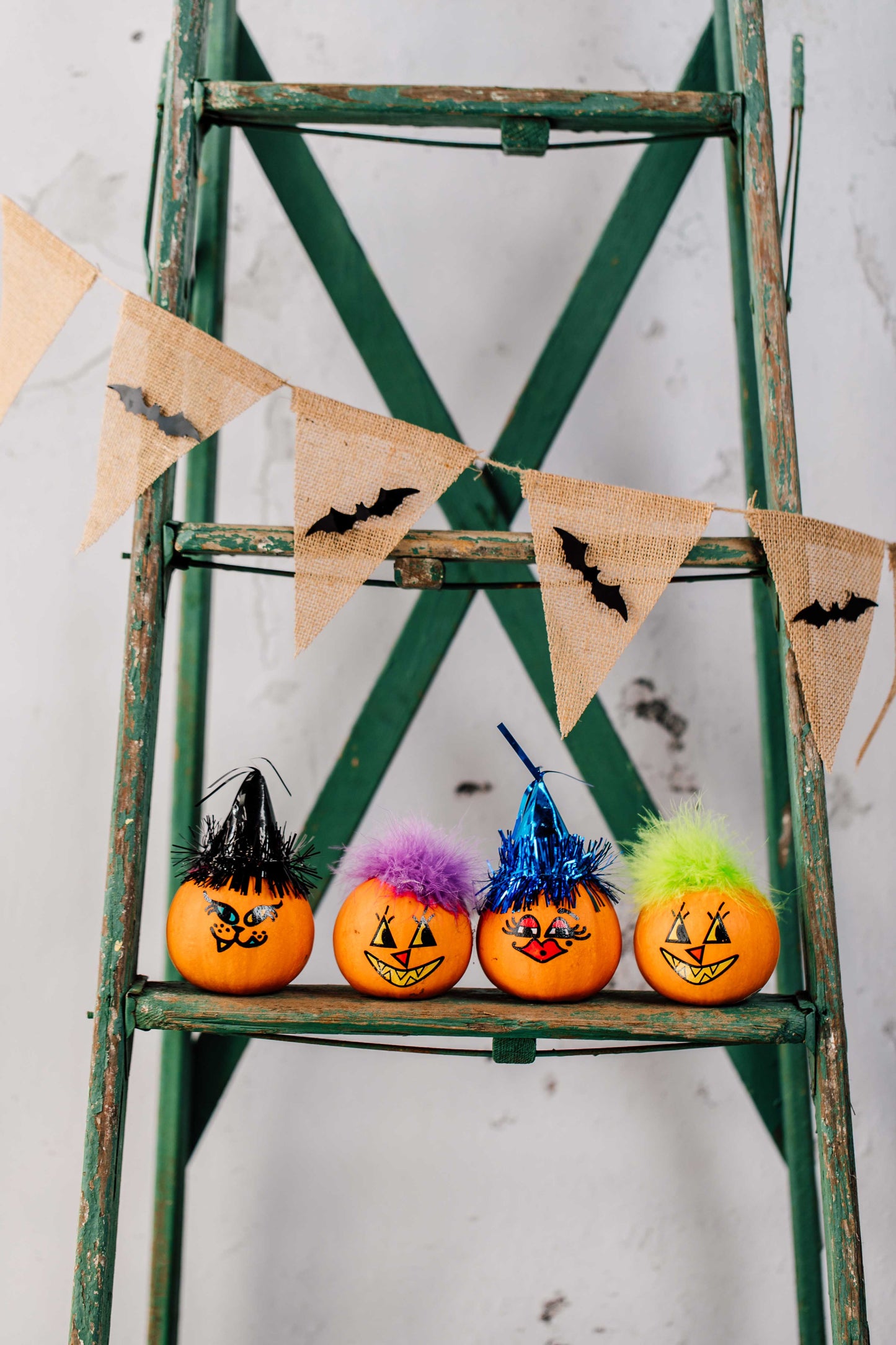 Decorative Halloween pumpkins with colorful faces on a green ladder with a banner.