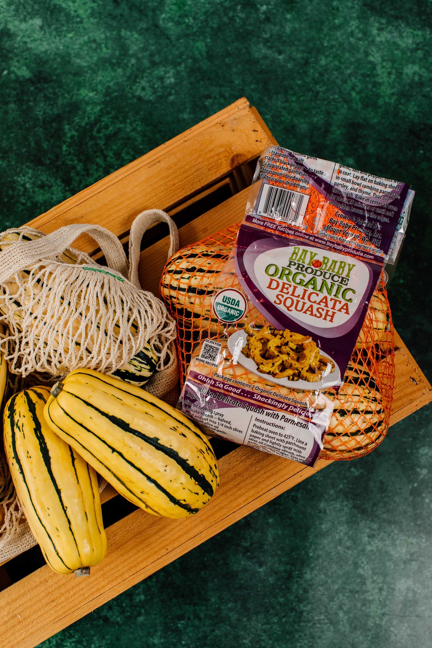 Packaged organic delicata squash with yellow squashes on a wooden surface
