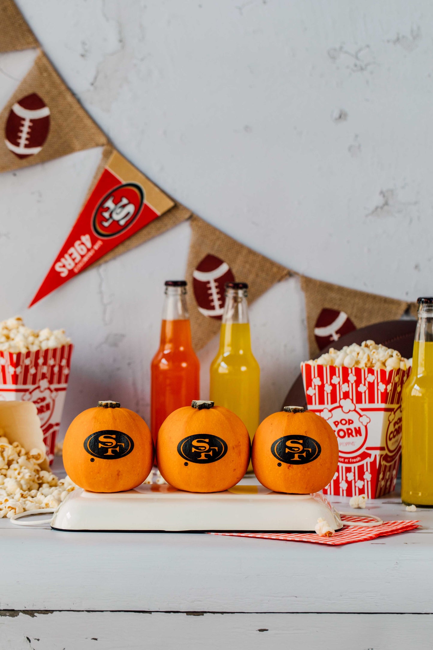 Pumpkin-themed drinks with sodas and popcorn on a table against a sports-themed backdrop.