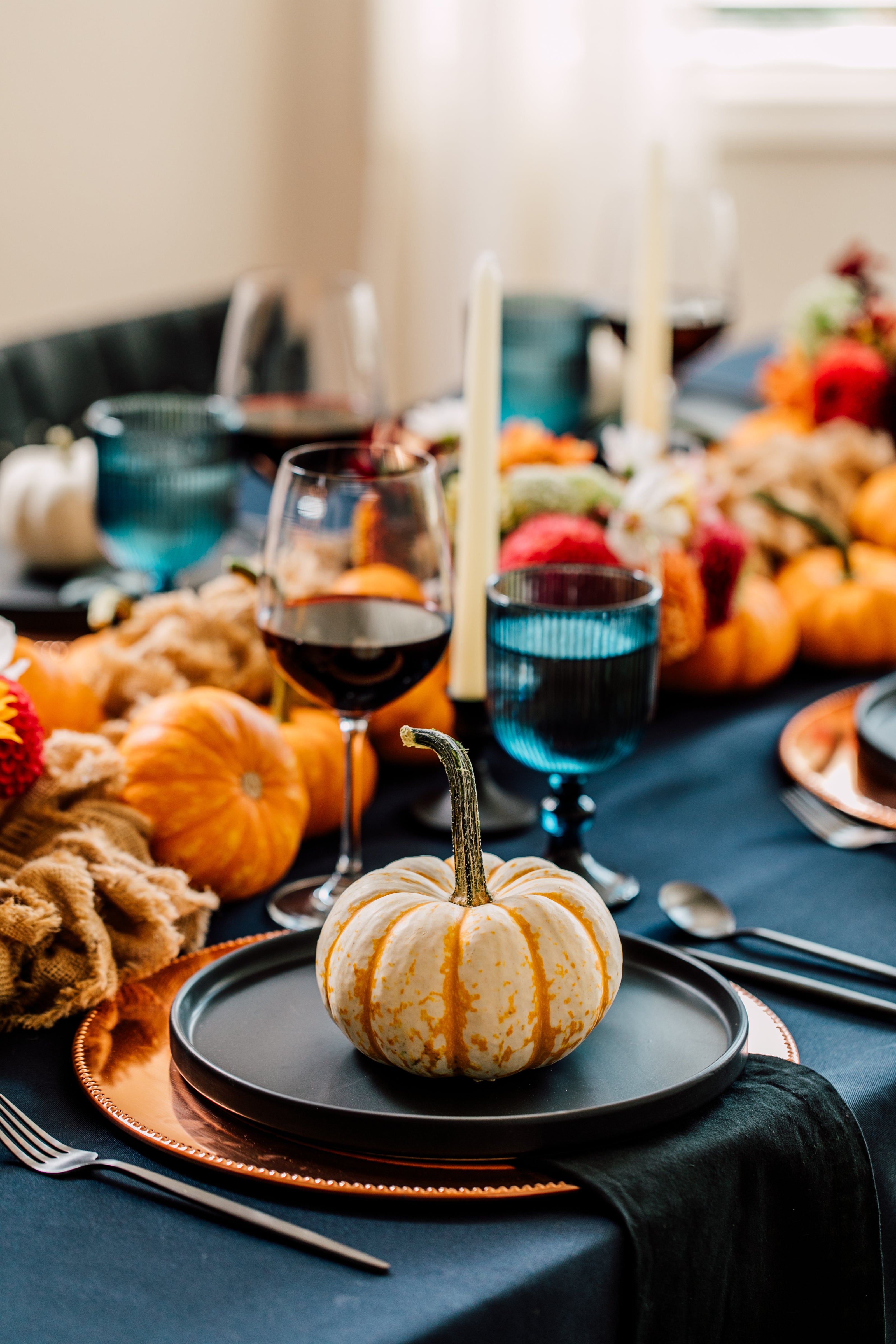 Decorative table setting with pumpkins, candles, and blue glasses on a dark tablecloth.