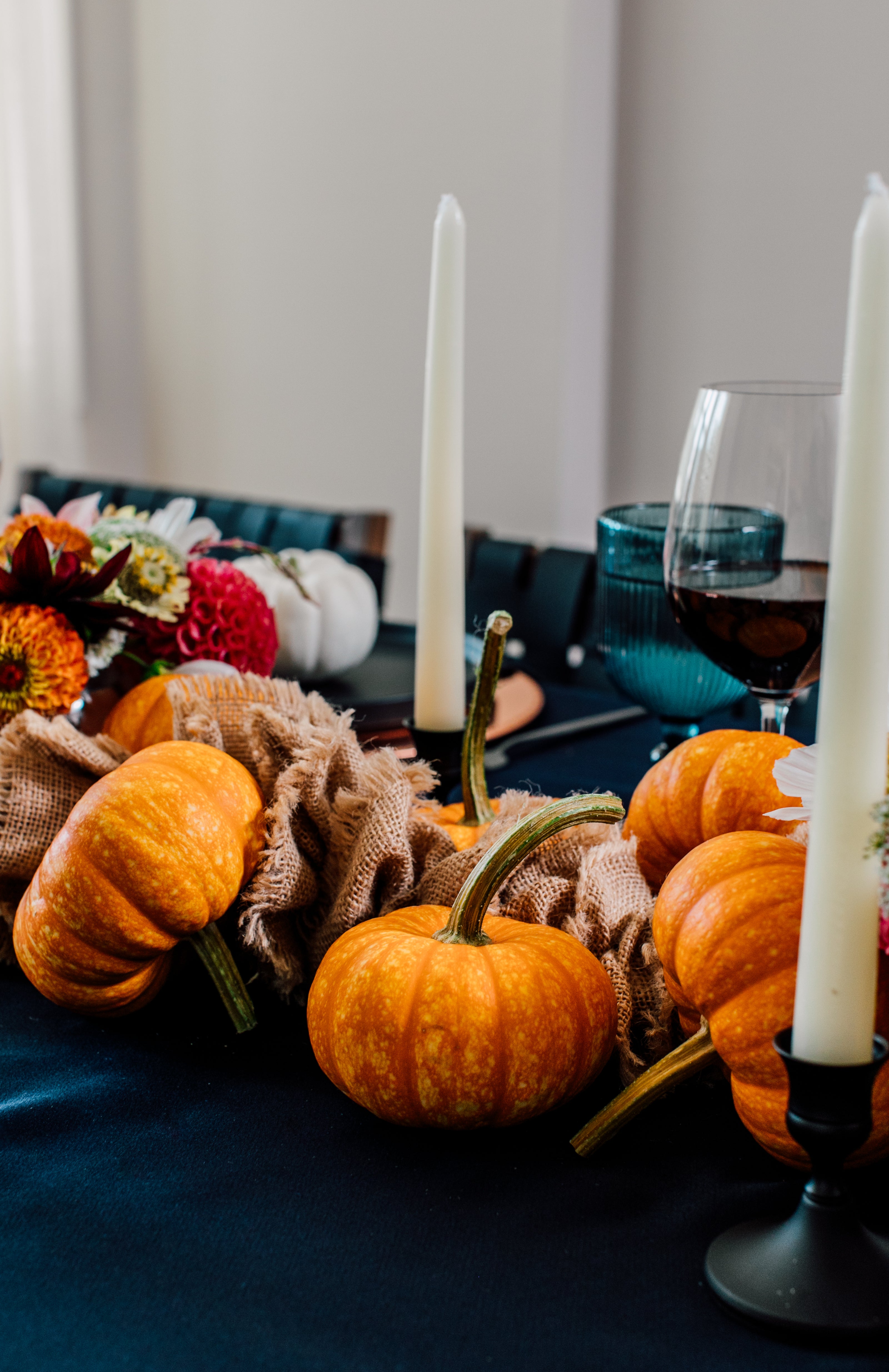 Decorative table setting with pumpkins, candles, and flowers on a blue tablecloth.
