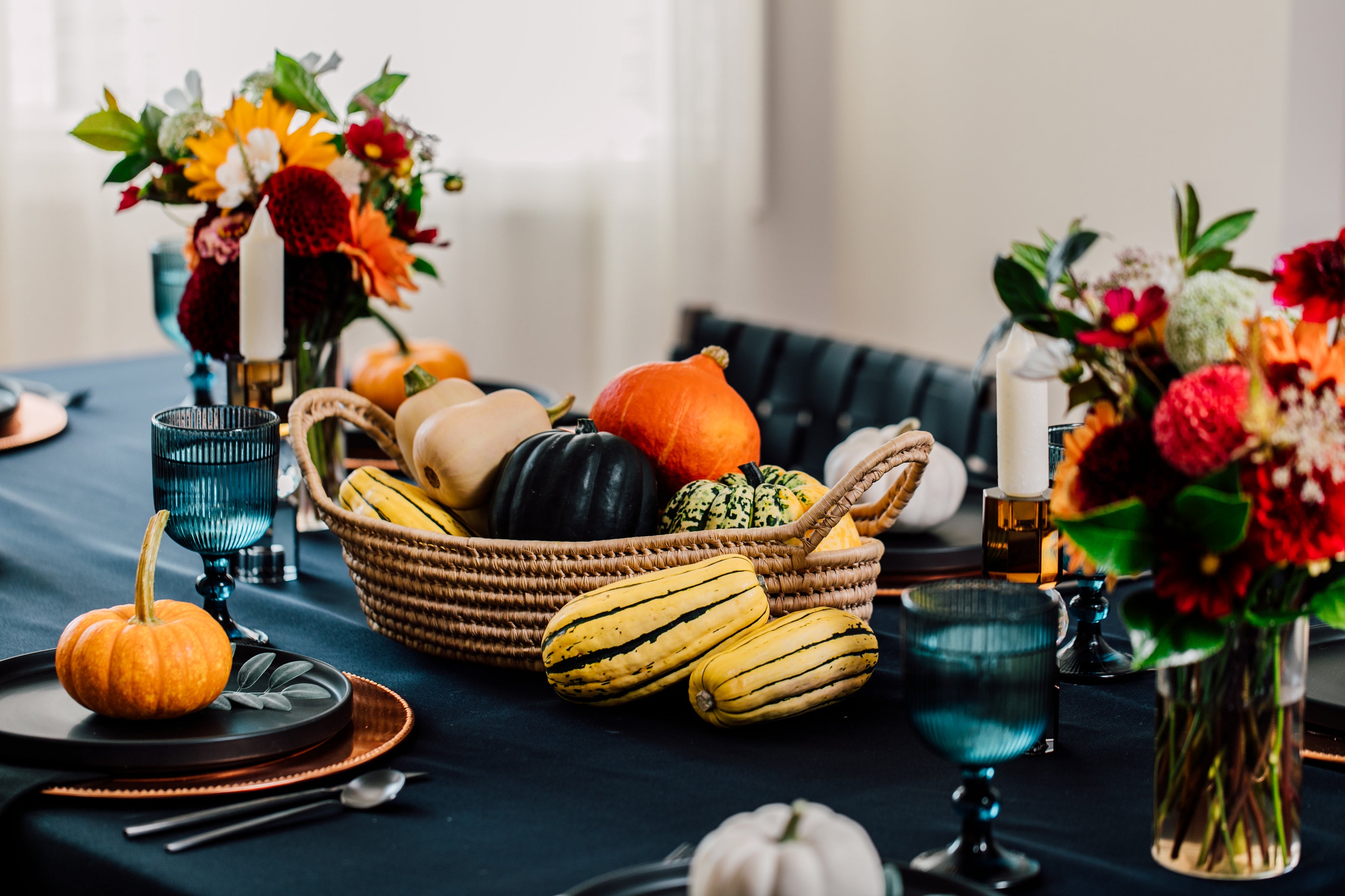 Decorative table setting with pumpkins, gourds, and floral arrangements on a blue tablecloth.