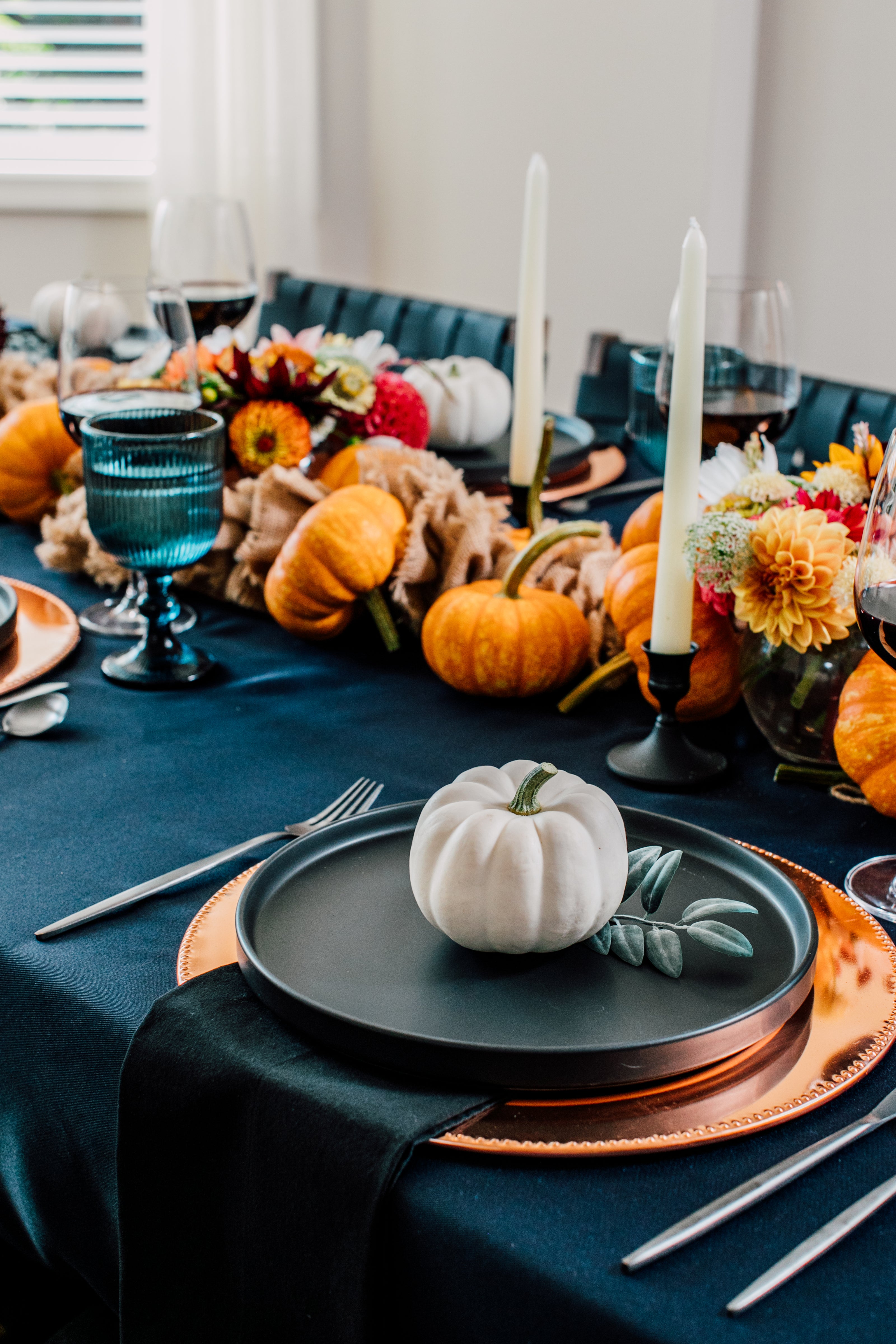 Decorative table setting with pumpkins, candles, and flowers on a blue tablecloth.
